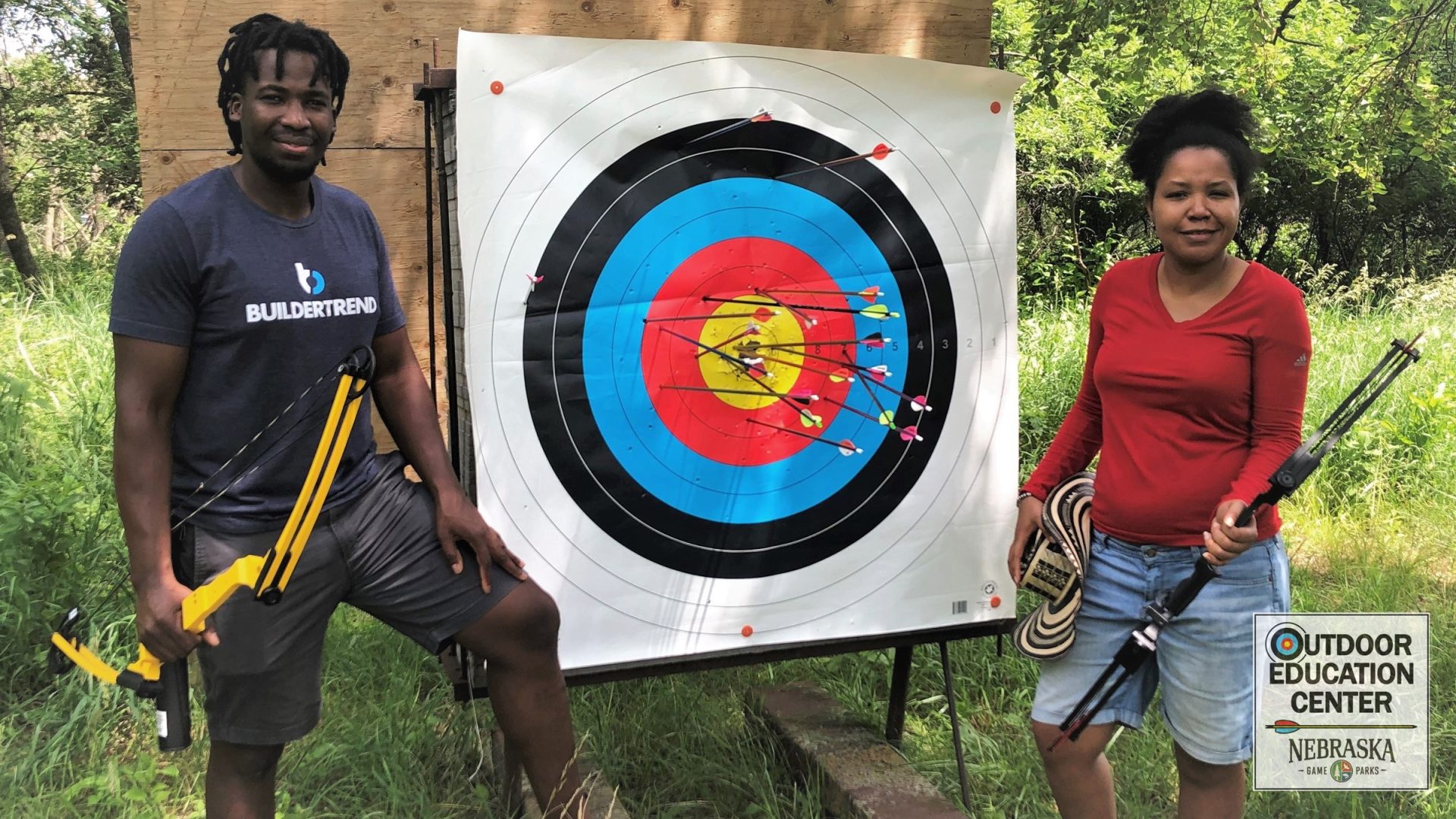 Two archers holding bows next to outdoor target