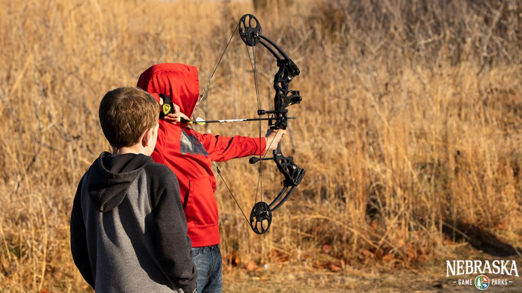 Two kids shooting archery outside.