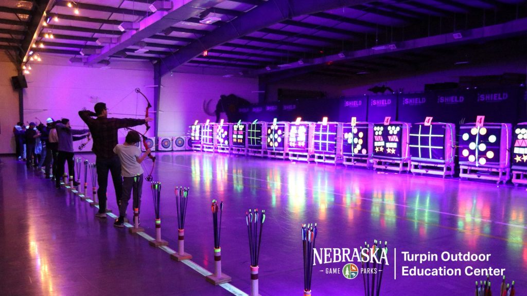 Indoor archery range with purple lighting and glowing targets