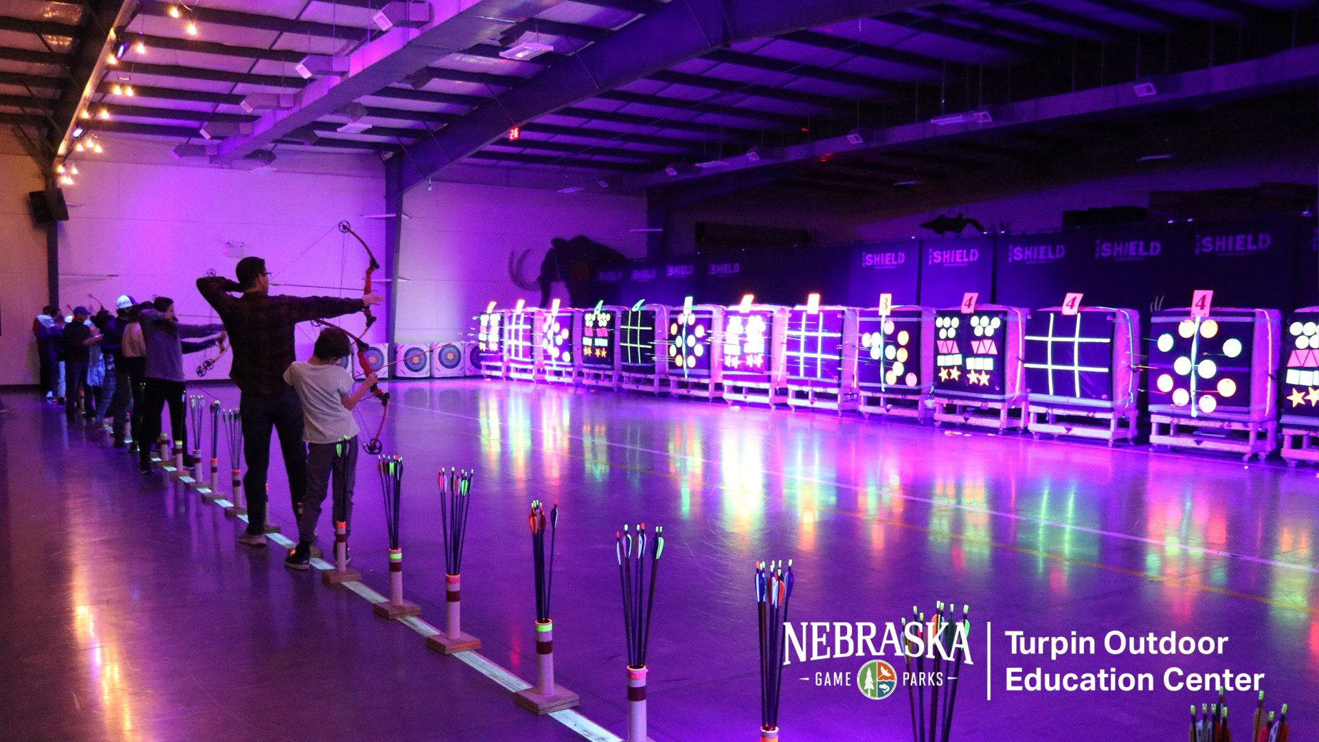 Indoor archery range with purple lighting and glowing targets