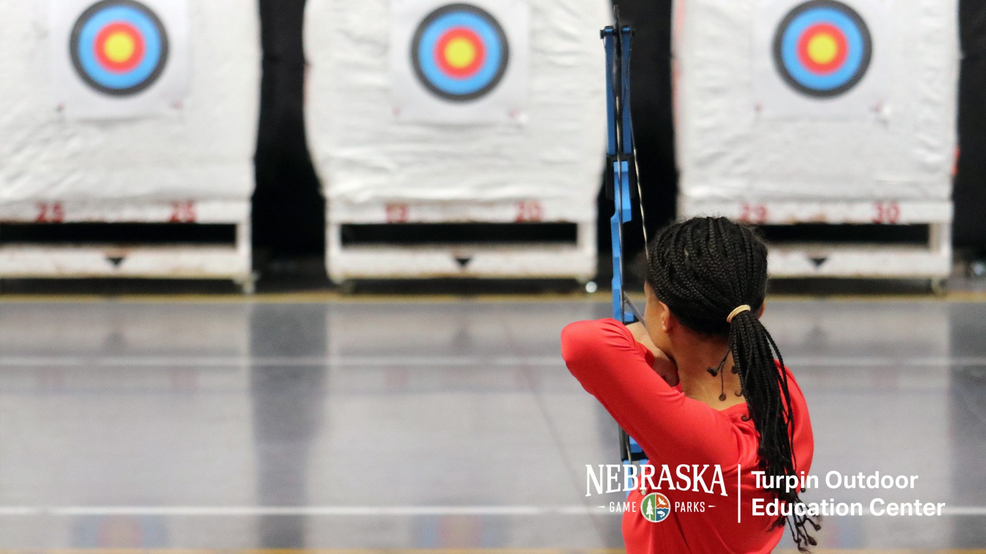 Woman aiming bow on indoor archery range