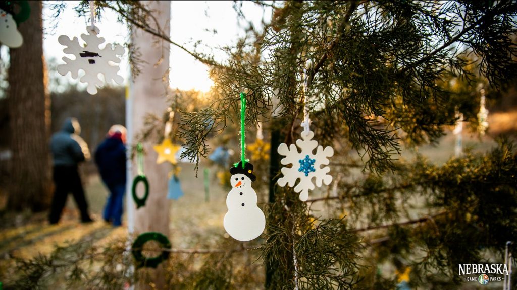 Christmas ornaments hang from a tree in a park.