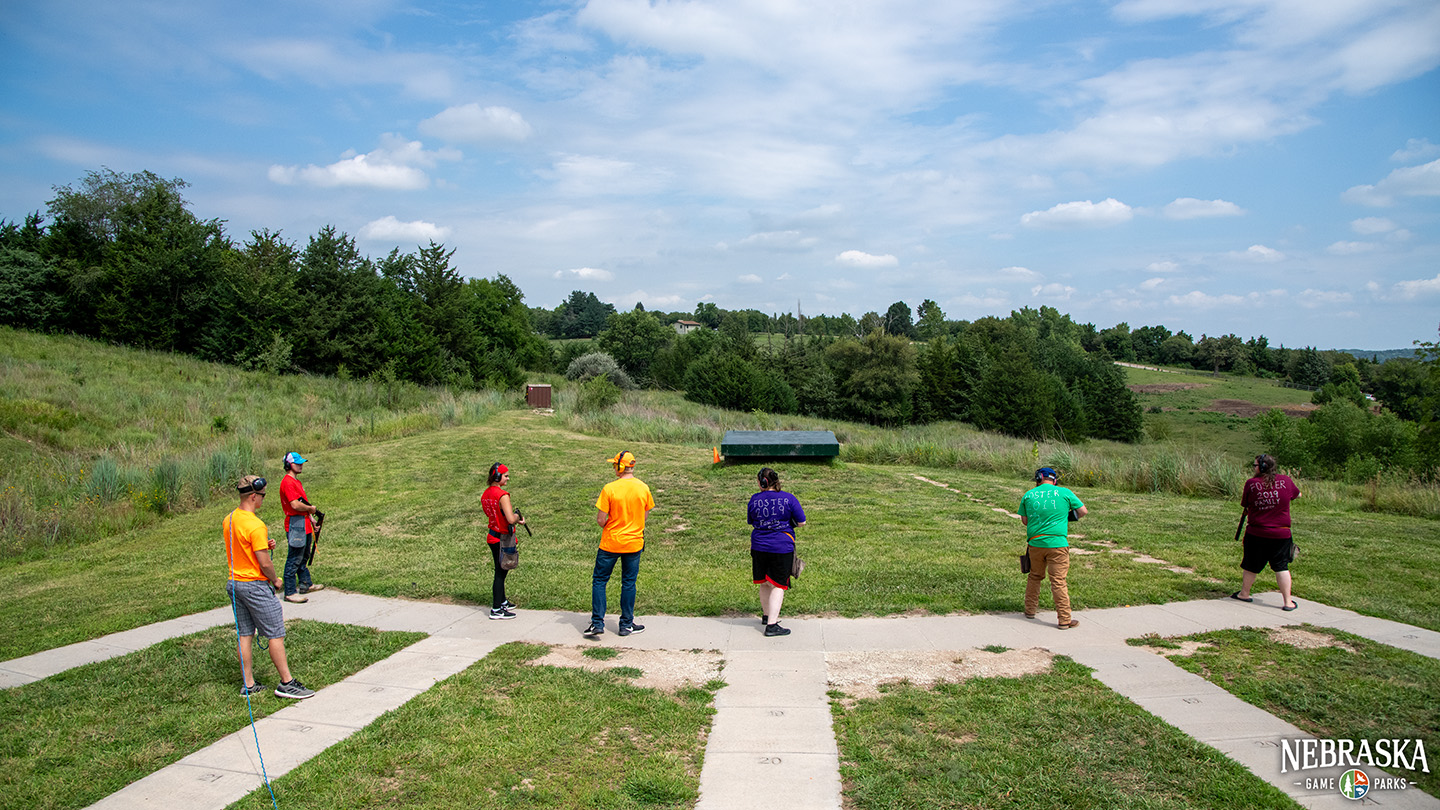 A group of people and instructors practice shotgun shooting on a range.