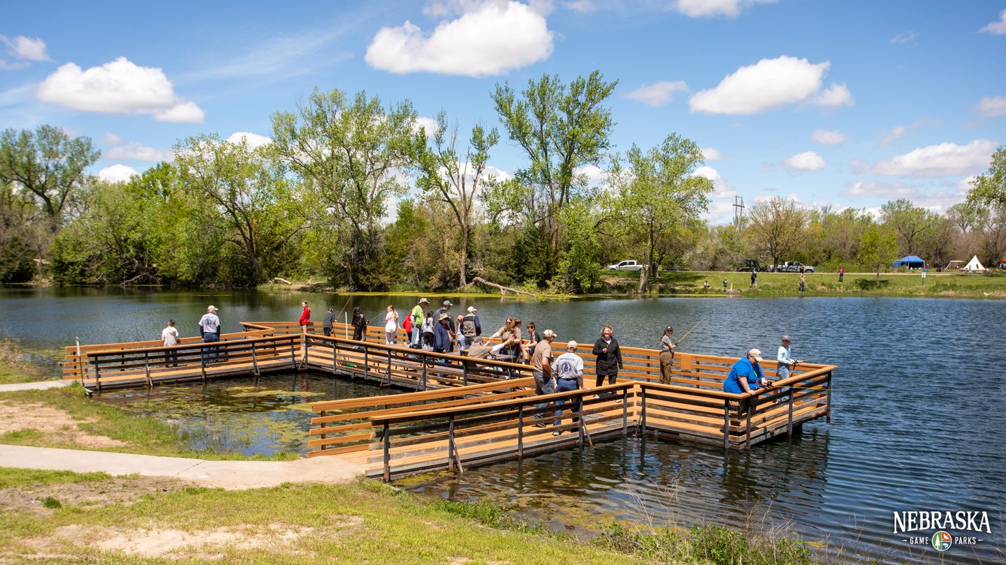 People fish off a dock at a lake on a summer day.