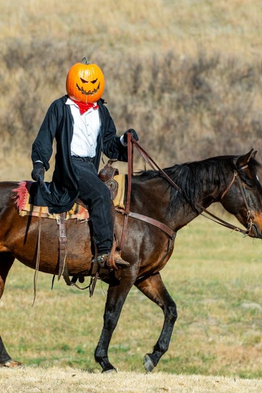 A man wearing a pumpkin head rides a horse on Halloween at a park.
