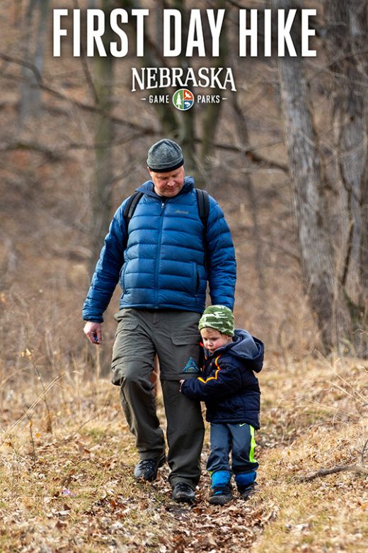 A father and son hike on a trail in a forest during winter.