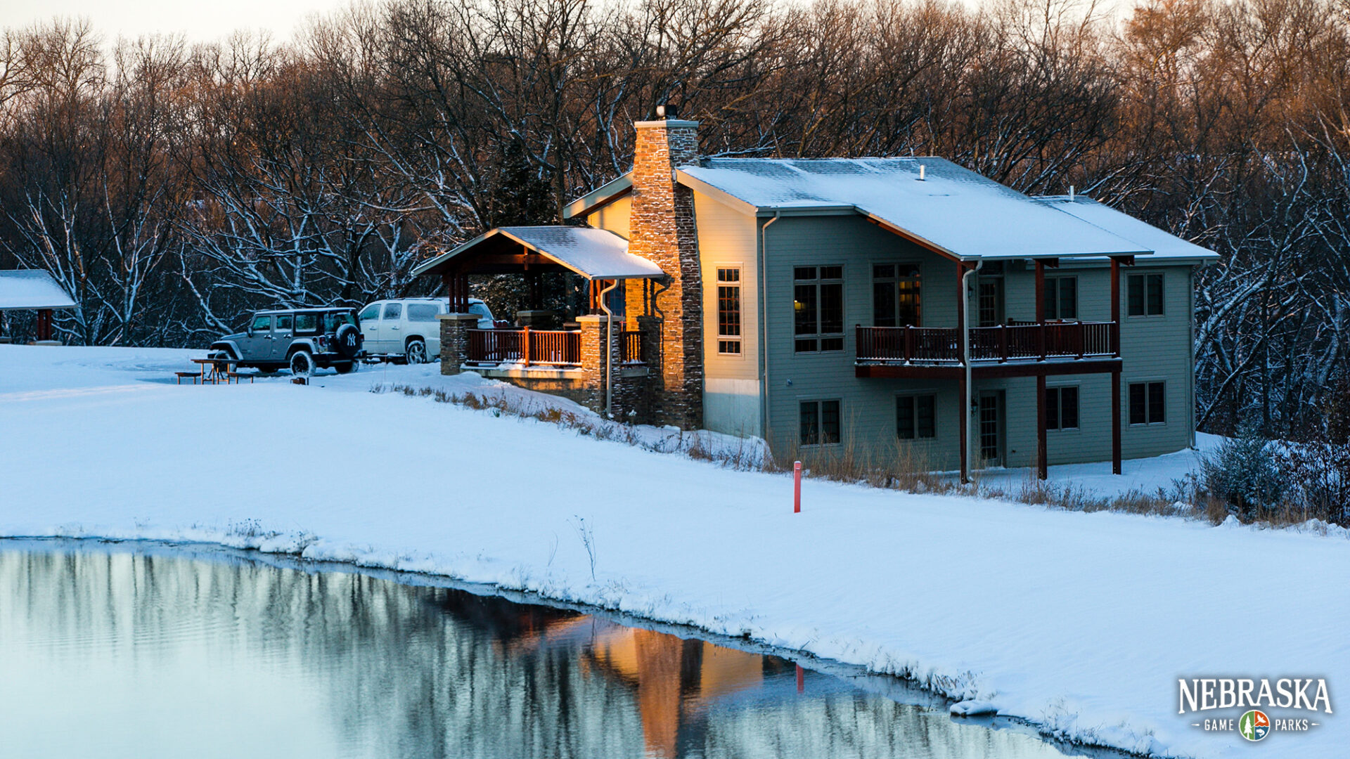 Winter scene of a cabin at Ponca State Park next to a pond.
