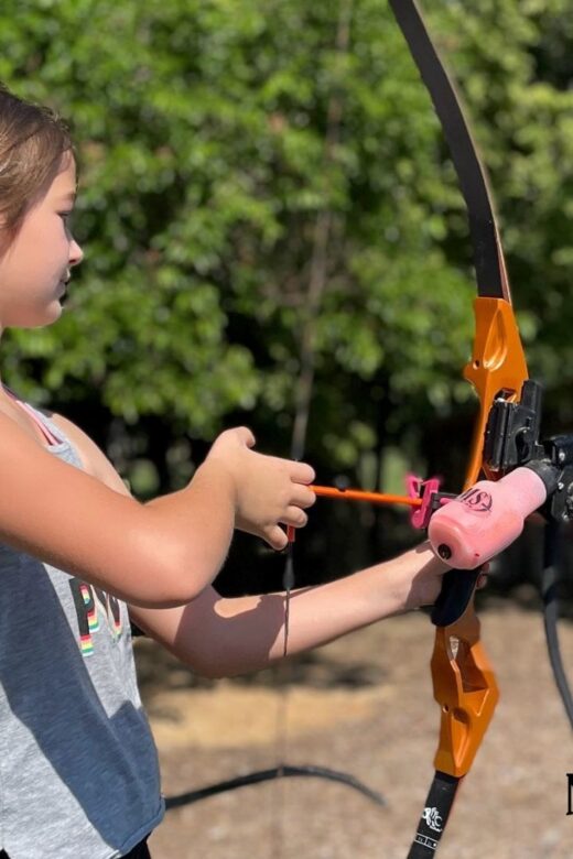 A girl shoots archery outdoors.