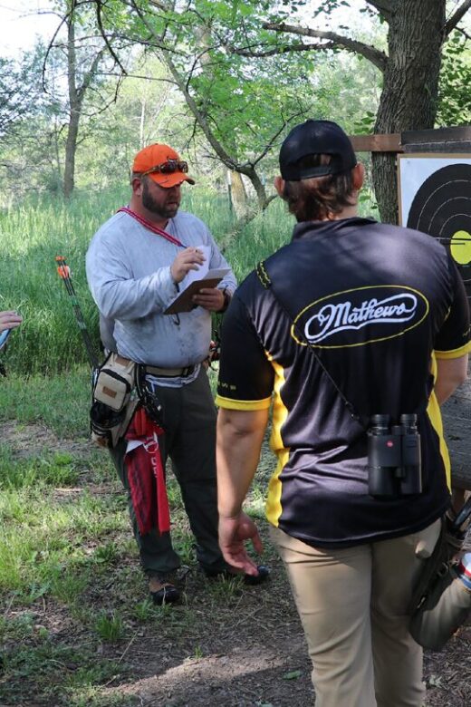 People participating in an outdoor archery competition in a forested area.