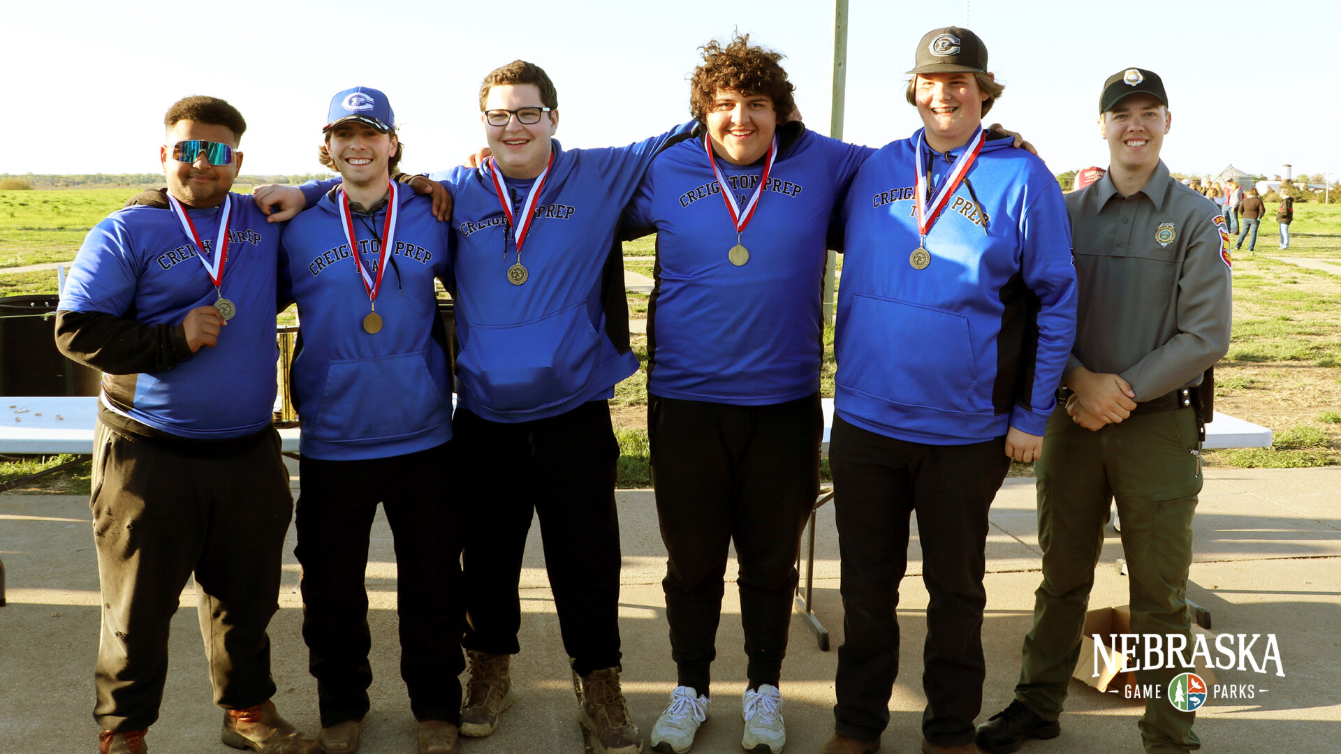 Team of 5 trap competitors from Creighton Prep posing with medals next to Conservation Officer