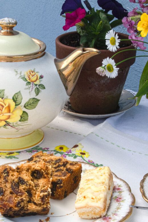 A vintage tea set on a table with flowers and desserts.
