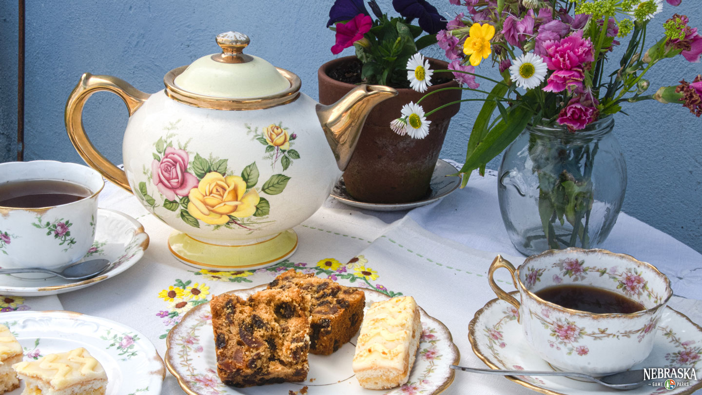 A vintage tea set on a table with flowers and desserts.