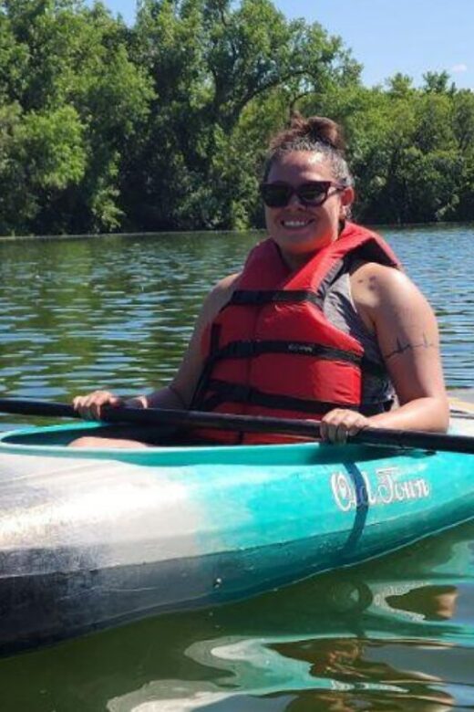 A woman kayaking in a lake wearing a life jacket.