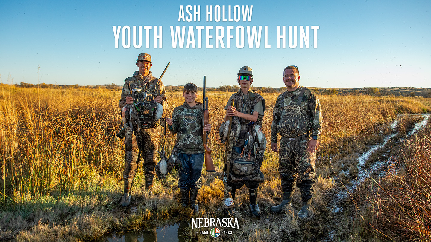 Three youth and one adult waterfowl hunter pose with harvests in a field.