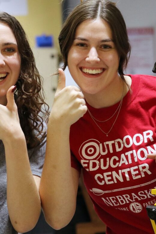 Two college students holding bows and giving a thumbs up for College Night on the range.