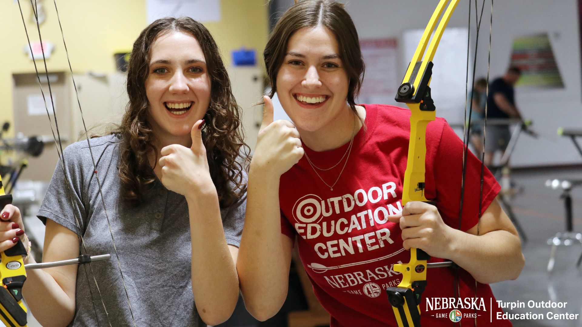 Two college students holding bows and giving a thumbs up for College Night on the range.