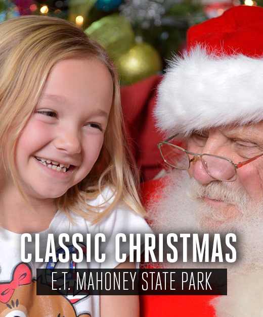 A smiling little girl sits on Santa's lap.